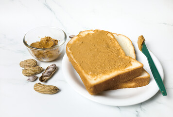 peanut butter on toast bread with nuts near green plastic knife at white table, top view