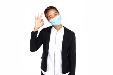 Asian businesswoman w surgical face mask in formal suit jacket, look at camera, fingers showing shows OK or ring-gesture, studio lighting isolated on white background, coronavirus, COVID19 concept


