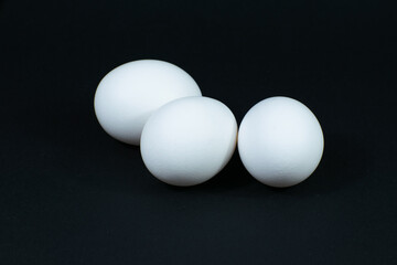 Three white chicken eggs on a black background.