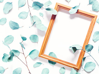 Composition with plants. Turquoise colored eucalyptus leaves isolated on a white background. Nearby is an empty wooden photo frame. Flat lay. Copy space.