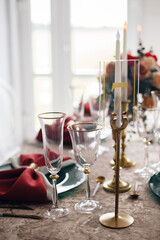A very nicely decorated wedding table appointments with rose-red beautiful decor with green plates and gold serviettes in light interior. Beautiful flowers on table in wedding day.
