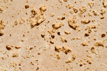 The popular travertine variety Travertine Classic is a warm beige color with pronounced pores and pattern heterogeneity. Deep pores, texture. Travertine stone floor tile abstract closeup background.