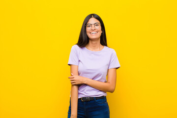 young pretty latin woman laughing shyly and cheerfully, with a friendly and positive but insecure...