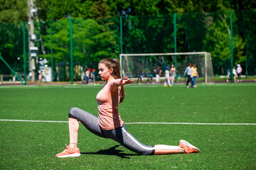 Attractive sporty young woman in sportswear doing stretching exercises on stadium. Fitness woman doing warm up workout.