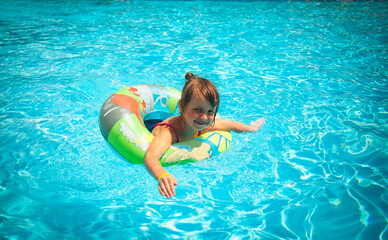 Pretty little girl in the outdoor pool at the resort. Summer holiday and happy carefree childhood concept.