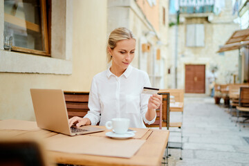 Working, traveling and online banking. Pay the bill. Beautiful young woman holding plastic credit card while siting in sidewalk cafe.