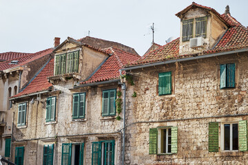 Fototapeta na wymiar Traveling by Croatia. Ancient architecture of Split old town. Old stone house with green shutters and res tiled roof.