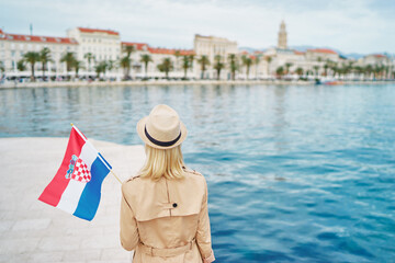 Enjoying vacation in Croatia. Young traveling woman with national croatian flag walking on Split...