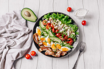 Cobb salad with chicken, avocado, tomatoes, eggs, bacon and cheese on a white wooden  table top view.
