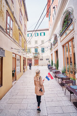 Enjoying vacation in Croatia. Young traveling woman with national croatian flag walking on Split Old Town.