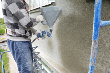 A building contractor is rendering, plastering, coating the exterior wall of a building using...