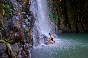 Fototapeta na wymiar Travel and nature. Young woman swimming in tropical waterfall pool.