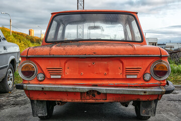 Bright red soviet retro car ZAZ or Zaporozhets. Old red rusty and dirty retro automobile back view.