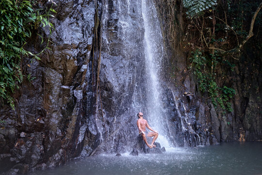 Happy young man relaxing under tropical waterfall  Vacation and relaxation.