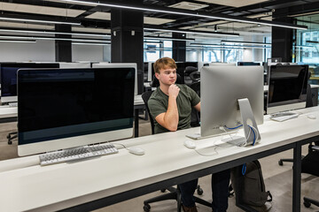 The concept of education, a young man sits at a computer, teaches students in the workshop, using a...