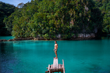 Vacation and activity. Young man enjoying blue tropical lagoon view standing on wooden springboard. Siargao Island, Philippines. © Loginova