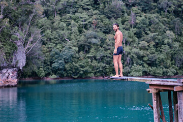 Vacation and activity. Young man enjoying blue tropical lagoon view standing on wooden springboard. Siargao Island, Philippines.