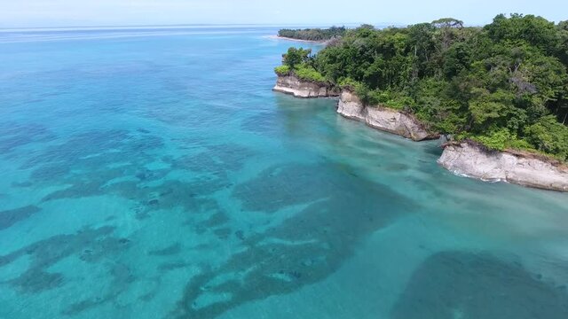 Forward Flying Aerial View of Escudo Island in Light Blue Colored Water with Coral Reefs, Rock Cliffs and Tropical Jungle Trees