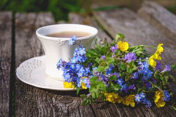 Herbal tea in a white vintage ceramic cup, fresh forget-me-not flowers on a wooden boards background