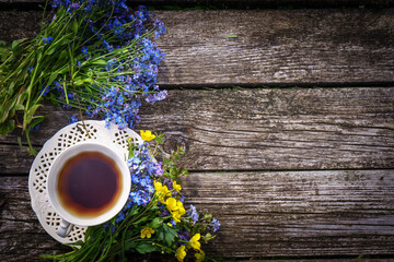 Herbal tea in a white vintage ceramic cup, fresh forget-me-not flowers on a wooden boards background