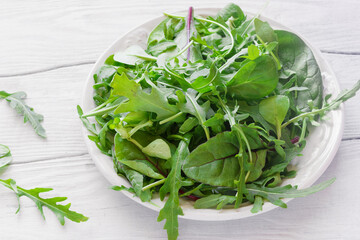 Fresh herbs from arugula, corn salad, chard and spinach in a plate on a white wooden table