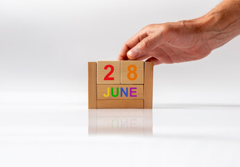 June 28 date on wooden calendar in colors of LGBTQ flag colors with male hand on white glossy...