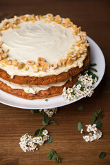 Carrot cake with hazel nuts and white flowers of meadowsweet on the wooden table