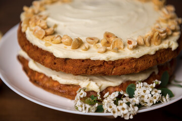 Carrot cake with hazel nuts and white flowers of meadowsweet on the wooden table