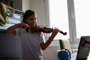 Cute child (little girl) playing violin and exercising at home. Remote learning from home. Video chat conference lesson. Adorable girl with musical instrument. © Nenad