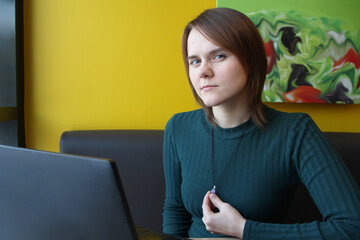 A girl with a pensive tense expression on her face sits, working at a laptop at a table in a cafe...