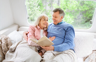 Loving mature couple reading book on bed in camper van during family trip