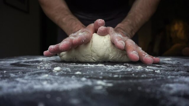Pizza dough making. Man's hands are kneading a dough with flour and a rolling pin on a black table. Slow motion (slo-mo, slow-mo).