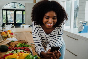 Beautiful woman with afro in the kitchen browsing mobile device