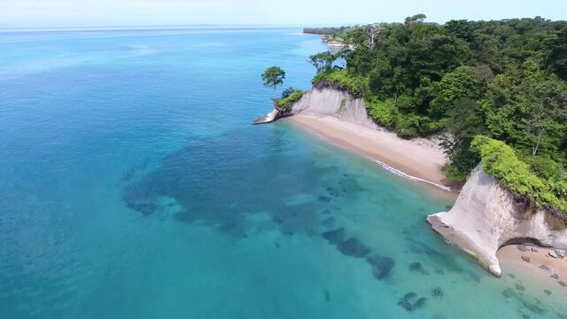 Forward Flying Aerial View of Escudo Island in Light Blue Colored Water with Coral Reefs, Rock Cliffs and Tropical Jungle Trees