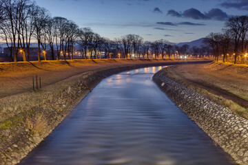 Blue hour Pirot city riverbank, streetlights and smooth, blur motion water of Nisava river