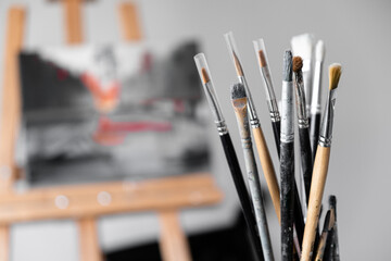 BRUSHES FOR drawing in a cup, on the back blurred background oil painting on an easel. red and gray tint. hobby.