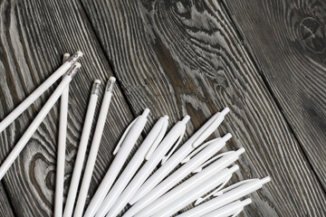 Several ballpoint pens and pencils in white. They lie on brushed pine boards painted in black and white.