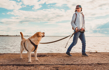A girl walks with a Labrador Retriever along the quay. Evening promenade with a dog