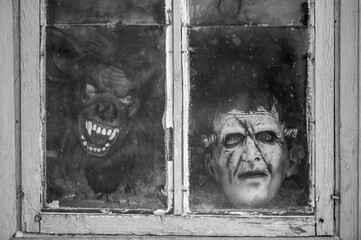 A child in a terrible monster mask peeks out of an old dirty window in winter