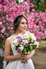 Girl with a bouquet stands at a flowering rose tree, wedding walk