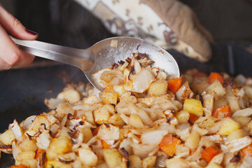 Large spoon stirs stewed vegetables on baking sheet