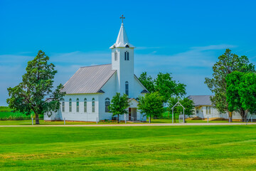 A small old fashioned white chapel sits in a peaceful green meadow in Texas.