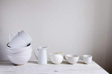 A set of white dishes on the table in the kitchen. Bowls, cups of various shapes, milk jugs, kitchen utensils for tea.