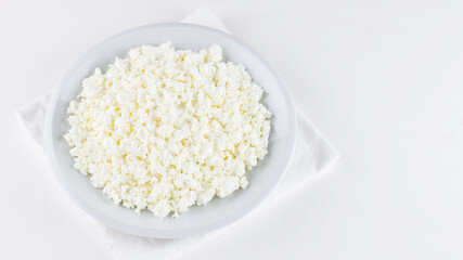 Cottage cheese in a plate on a white background. Cottage cheese on a white napkin. Top view. Copy space
