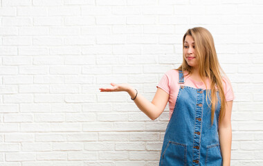 young blonde woman feeling happy and smiling casually, looking to an object or concept held on the...