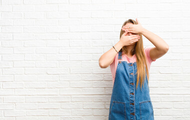 young blonde woman covering face with both hands saying no to the camera! refusing pictures or...