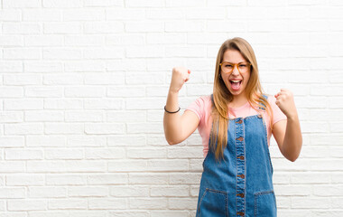 young blonde woman feeling happy, positive and successful, celebrating victory, achievements or...