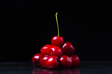 Red cherry pyramid. Red cherries folded in the form of a pyramid. At the very top is a cherry with a green stem. Cherry on a black background