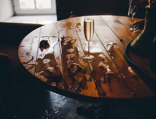 Spilled wine on a wooden table in a cafe and a lone glass of champagne. The consequences of stormy fun.