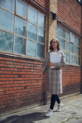 Young business woman walking by a nice old New Yorker building with paperwork in hands looking...